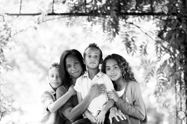 A mother and three children hug under a leafy archway as part of their London family portrait shoot.