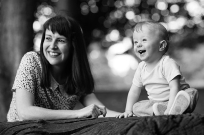 A mother and her baby sit on a log in a park.