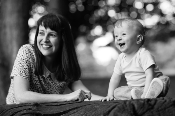 A mother and her baby sit on a log in a park.