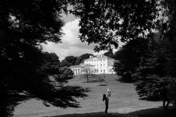 A mother holds up her baby with Kenwood House in the background.