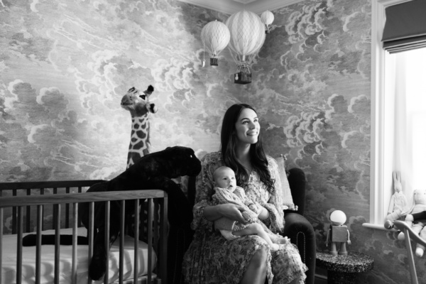 A mother holds her baby in a nursery chair, with a cot and toy giraffe next to her.