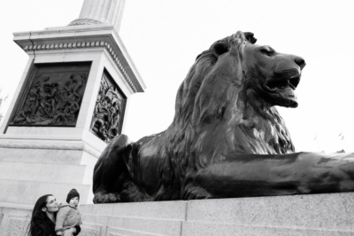 A mother and baby in Trafalgar Square, London, near Nelsons Column and a stone lion.