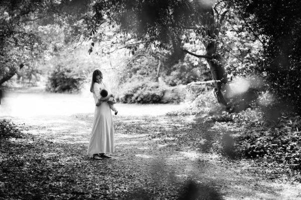 A mother holds her baby under trees.