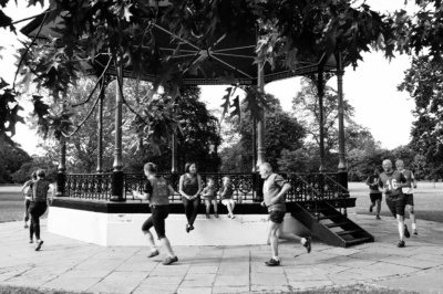 A mother and her two children on a bandstand while people run past.