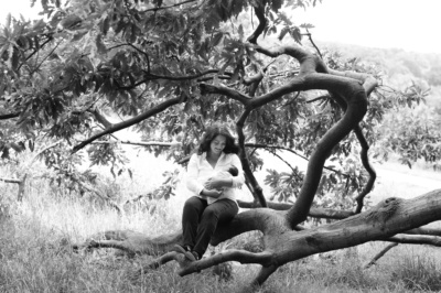 Mother cradles newborn sitting on a tree branch.