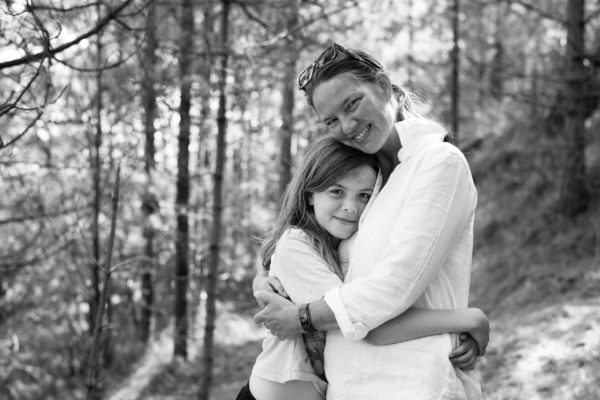 A mother and daughter hug each other in woodland.