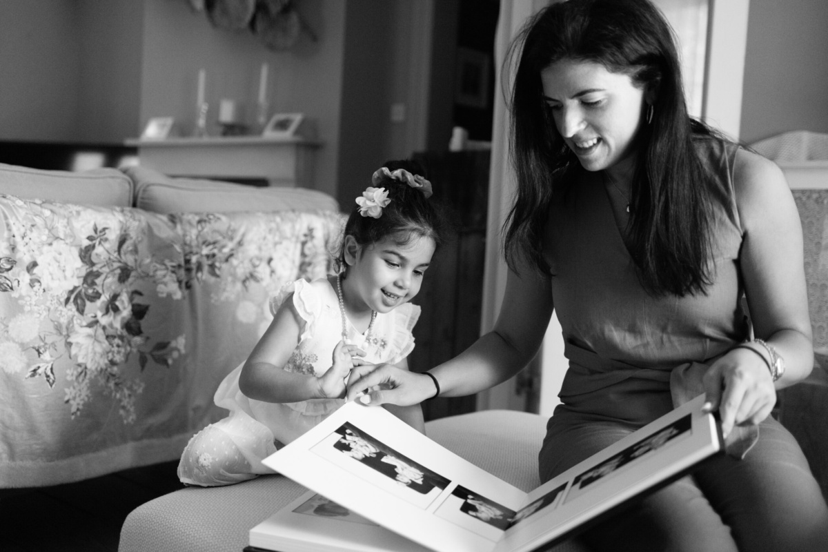 A mother and daughter look through a family album of black and white portraits.