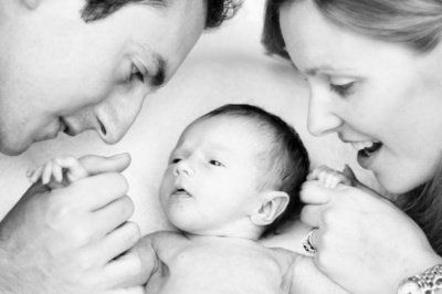 A mother and father hold hands with their newborn baby.