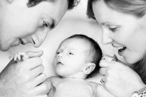 A mother and father hold hands with their newborn baby.