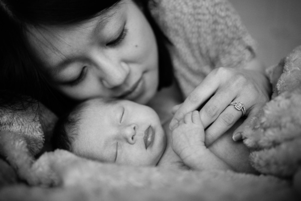 Mother holds hand of sleeping newborn child.