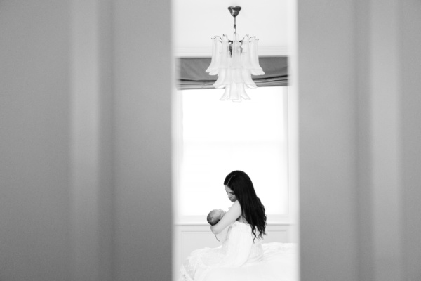 Mother holds newborn baby, seen through a gap between doors.