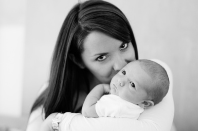 A mother kisses the cheek of their newborn baby.