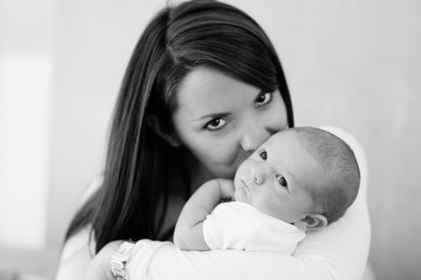 A mother kisses the cheek of their newborn baby.