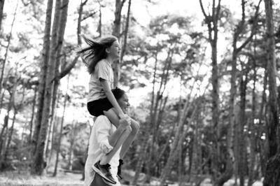 A mother piggybacks her daughter through woodland.