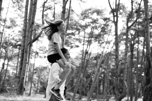 A mother piggybacks her daughter through woodland.