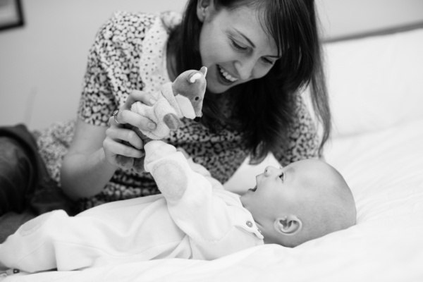 A mother plays with their baby and a soft toy.