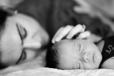 A mother strokes the head of her sleeping newborn.