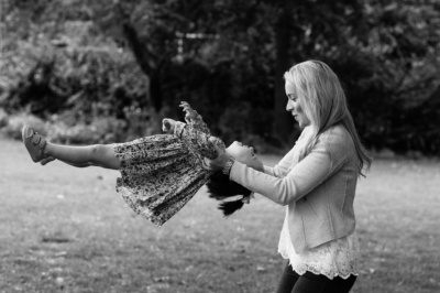 A mother swings her daughter under a tree.