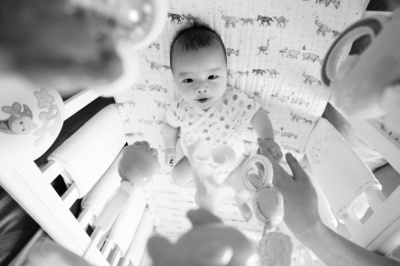 A newborn baby in its crib plays with its toys.