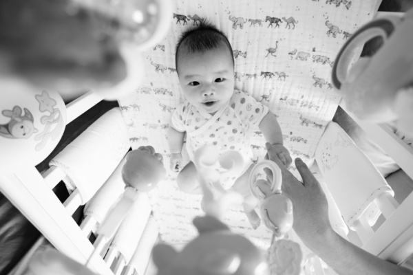 A newborn baby in its crib plays with its toys.