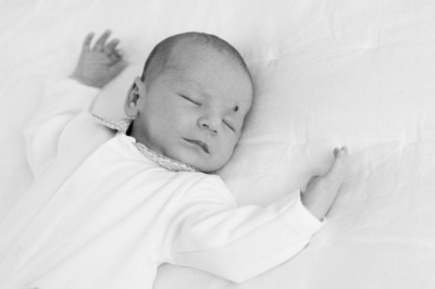 A newborn baby sleeps on a bed, arms outstretched.