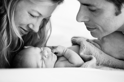 A portrait of parents and their newborn, wrapped in a knitted blanket.