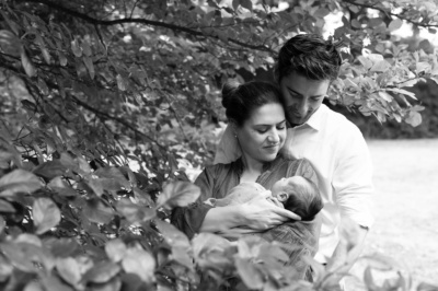 Parents hold their newborn in the shade of a tree.