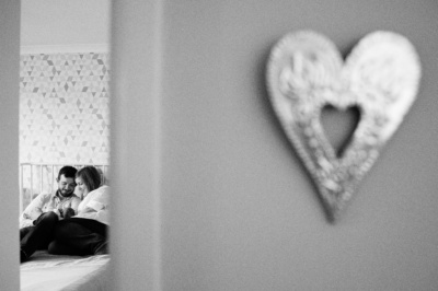 Parents hold their newborn, as seen through a doorway with a heart on the wall.