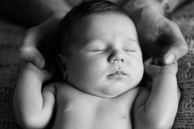 A newborn sleeps while their parent holds their hands.