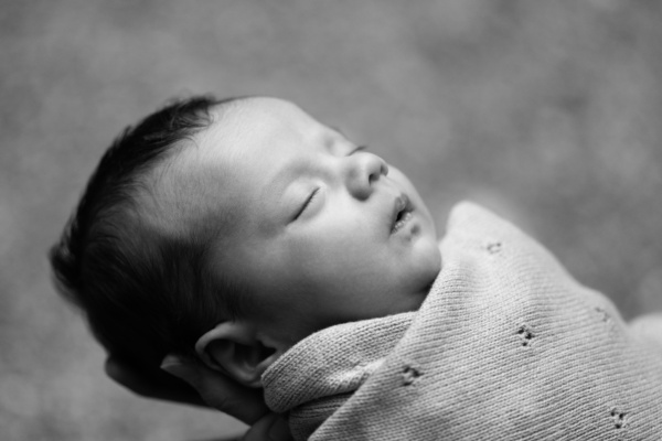 A newborn sleeps while swaddled in a knitted blanket.