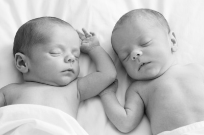 Newborn twins sleep together on white bedding.