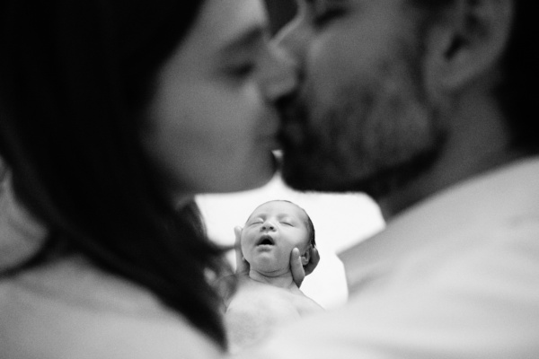 Parents kiss while holding their newborn baby.