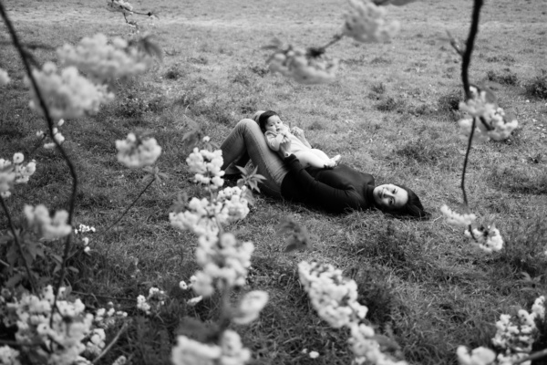 A parent and baby lie on the grass, surrounded by cherry blossom.