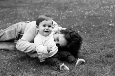 A parent and their baby giggle on the grass.