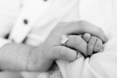 Parents hold their newborn's hand, showing the difference in size.