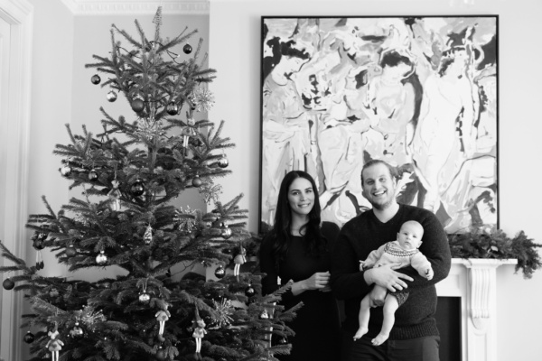 A mother, father and baby pose next to their Christmas tree for portraits.