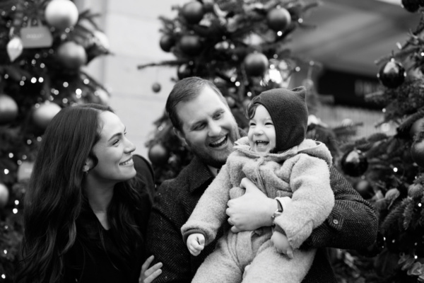 Parents and their baby with a background of Christmas trees iin Covent Garden, London.