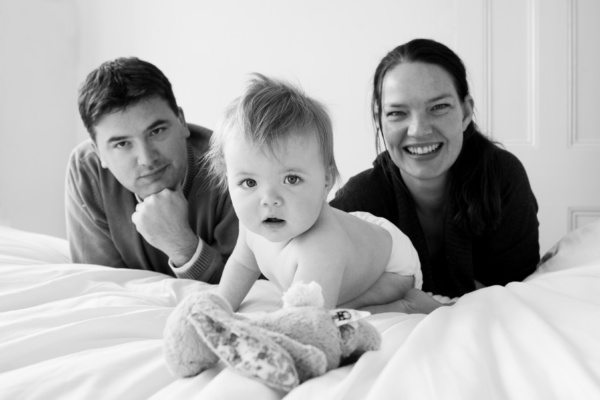 Parents and their baby lie on a bed together.