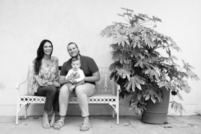 Parents and their baby on a garden bench next to a plant.