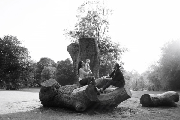 Parents and their baby sit together on a felled tree.