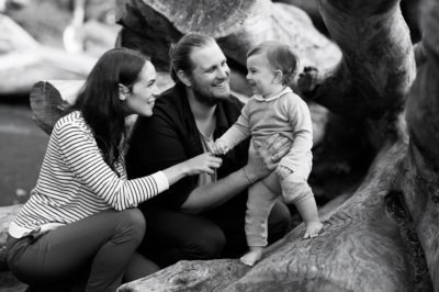 Parents and their baby smile together in black and white portraits.