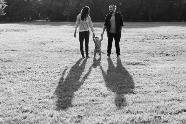 Parents and their baby walk across grass.