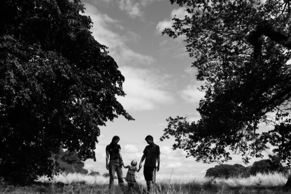 Parents and their child walk through a grassy field.