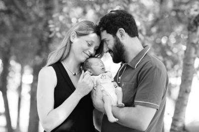 Parents cuddle their newborn in an outdoor portrait.