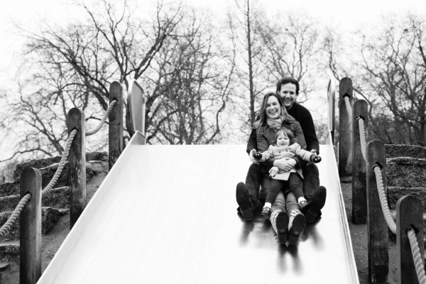 Parents and their daughter go down a slide together.