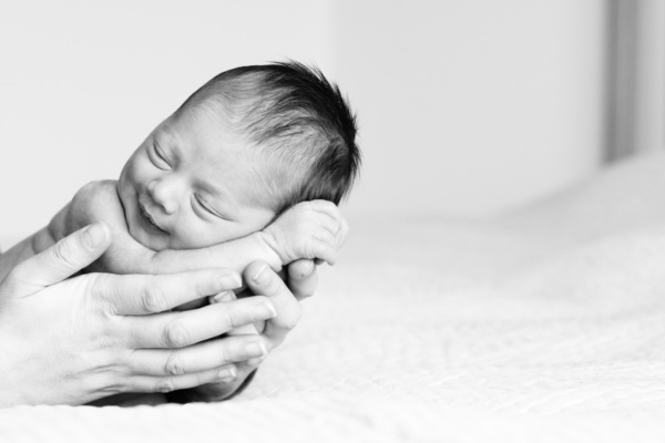 A parent holds both hands around a sleeping newborn baby.