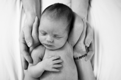 Parents hands support a sleeping newborn baby.