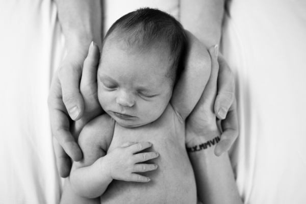 Parents hands support a sleeping newborn baby.