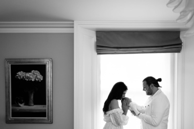 Parents hold their newborn, framed by a window.