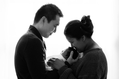 Parents hold their newborn between them as the mother kisses their head.